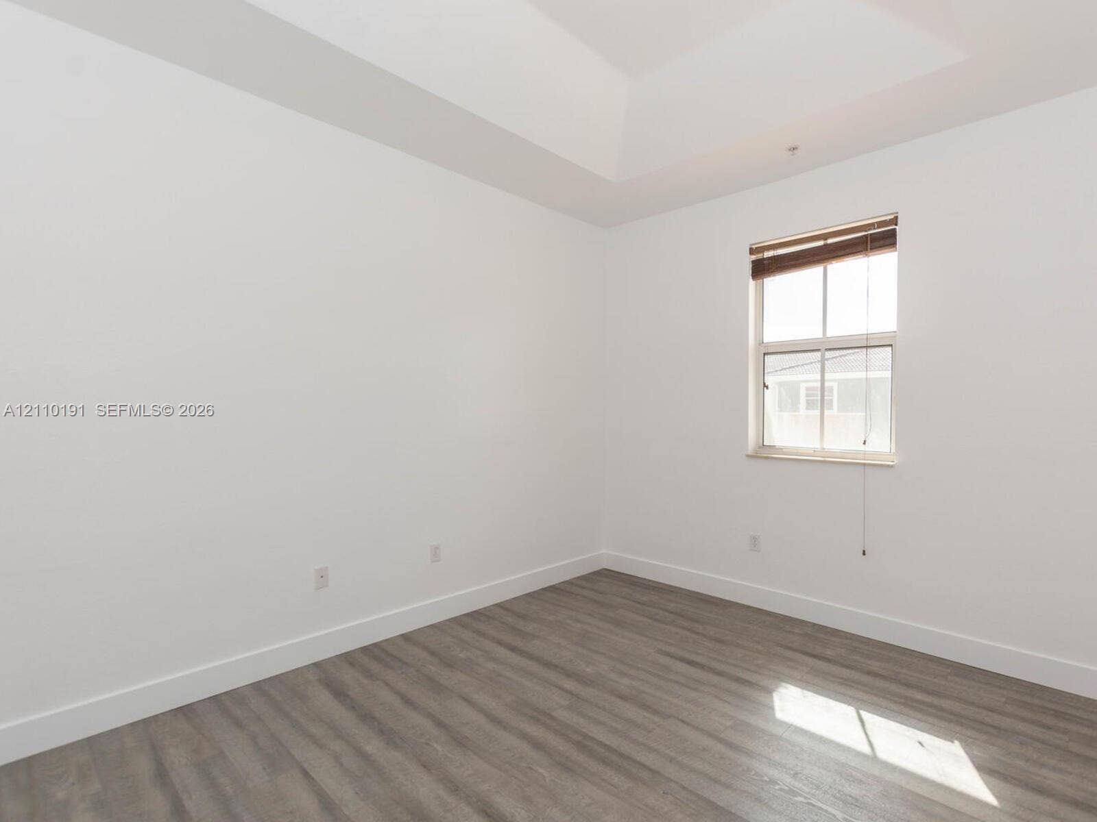 8999 NW 107 Court, #218-1, Miami, Miami, FL 33178 Room featuring a tray ceiling, wood-finish flooring, and a window with integrated blinds