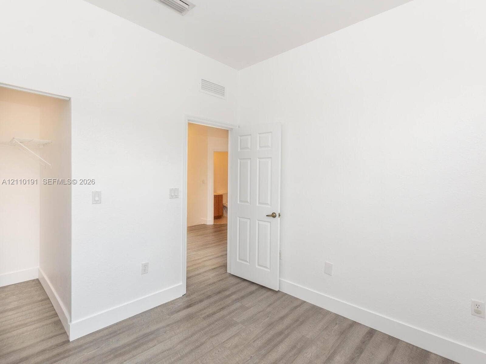8999 NW 107 Court, #218-1, Miami, Miami, FL 33178 Neutral interior featuring wood-finish flooring, a six-panel door with a metallic knob, and an open-access closet with a built-in wire shelf