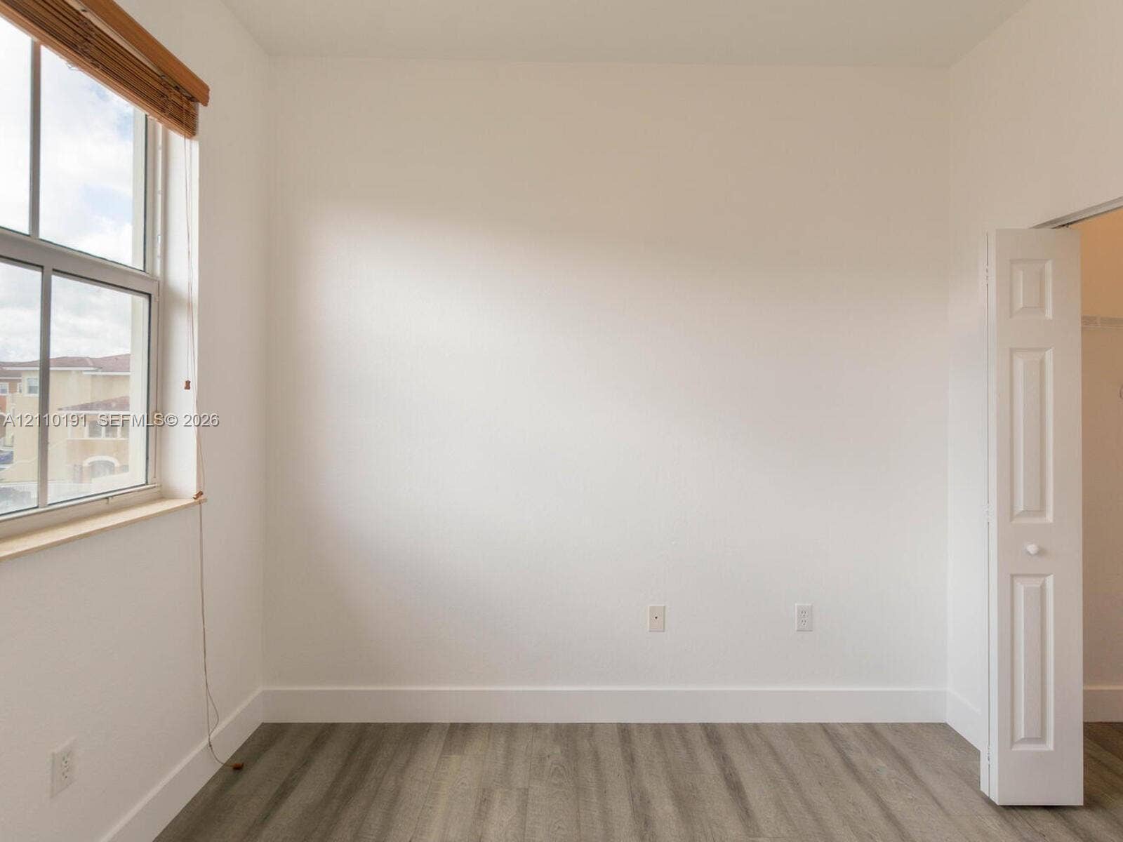 8999 NW 107 Court, #218-1, Miami, Miami, FL 33178 Neutral-toned interior space featuring wood-finish flooring, a multi-pane window with wood-trim blinds, and a paneled bifold closet door