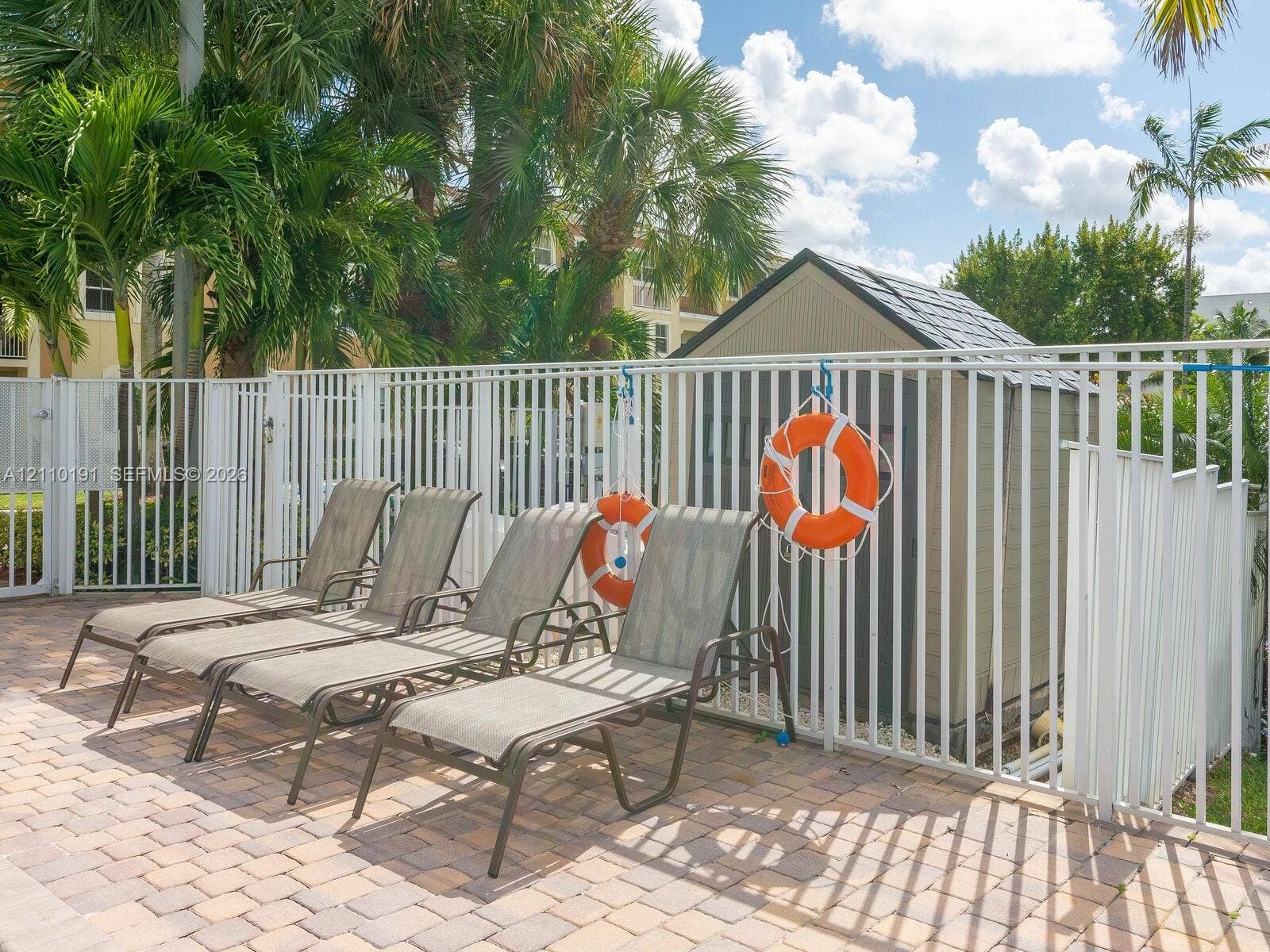 8999 NW 107 Court, #218-1, Miami, Miami, FL 33178 Paver patio featuring a perimeter metal fence, a utility shed, and mature palm trees
