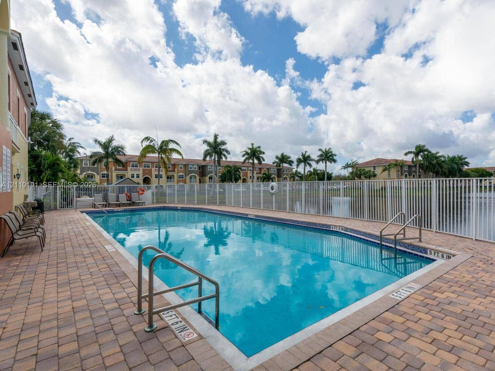 8999 NW 107 Court, #218-1, Miami, Miami, FL 33178 In-ground swimming pool with dual stainless steel entry railings, perimeter paver decking, and white metal safety fencing