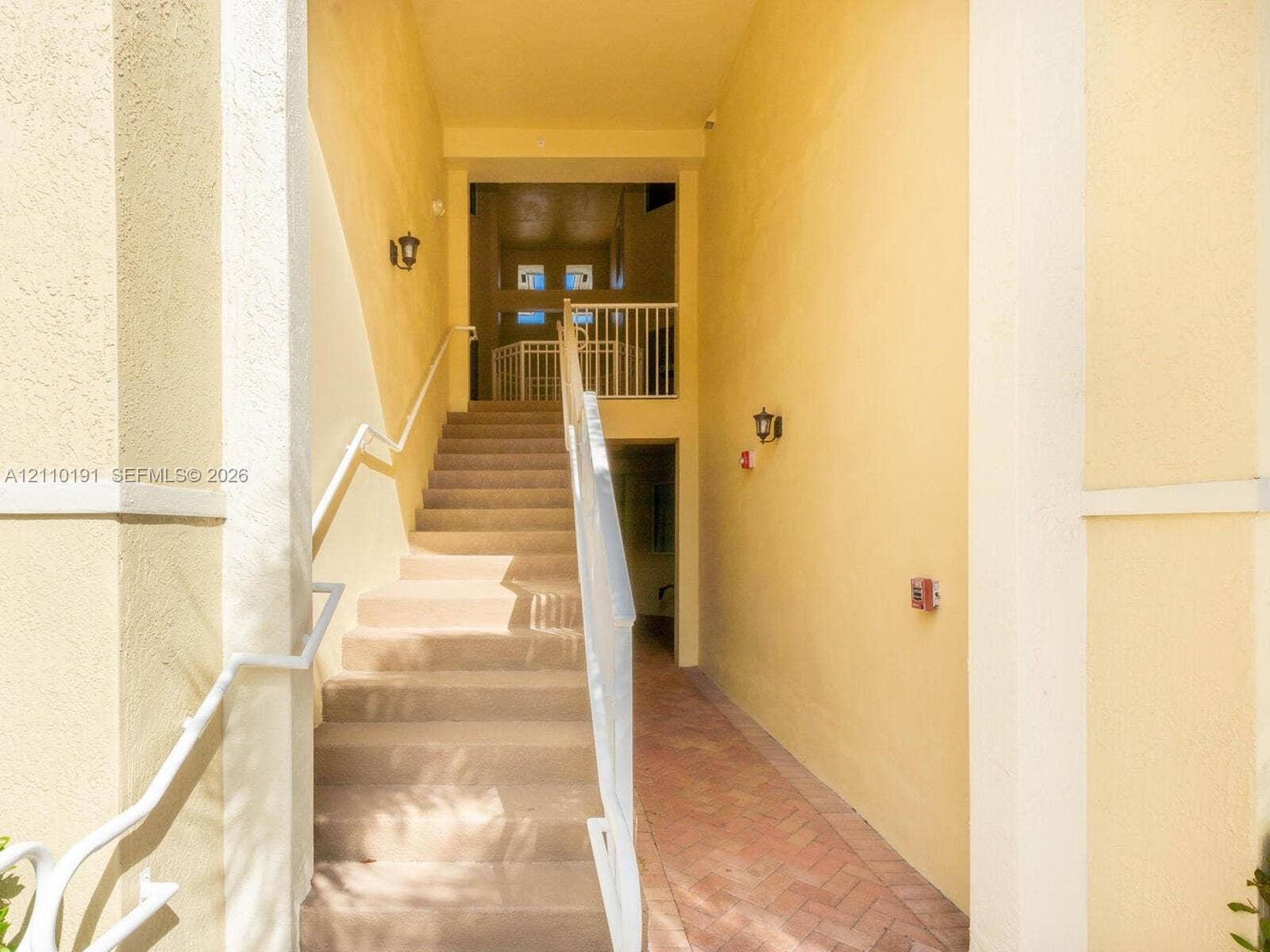 8999 NW 107 Court, #218-1, Miami, Miami, FL 33178 Exterior staircase featuring stucco walls, a herringbone-pattern brick pathway, and white metal railings