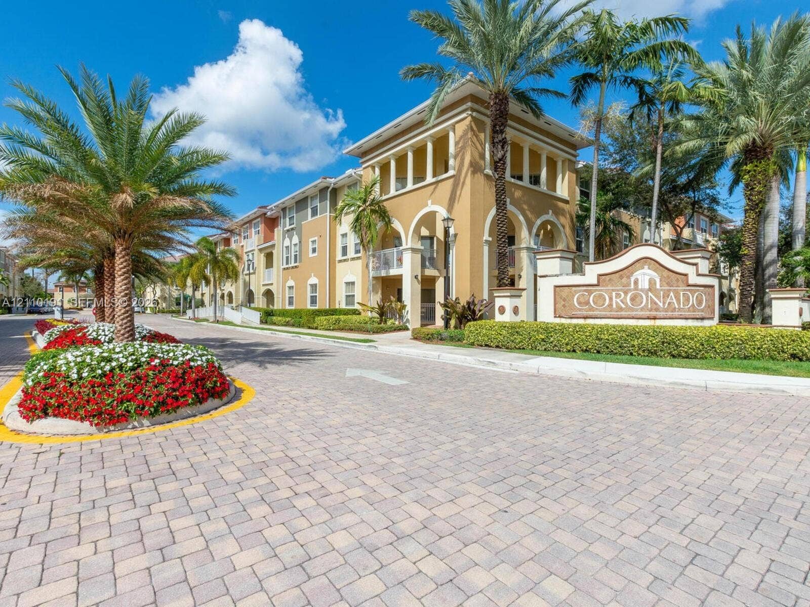 8999 NW 107 Court, #218-1, Miami, Miami, FL 33178 Stucco exterior featuring arched architectural detailing, paved stone driveway, and established tropical landscaping