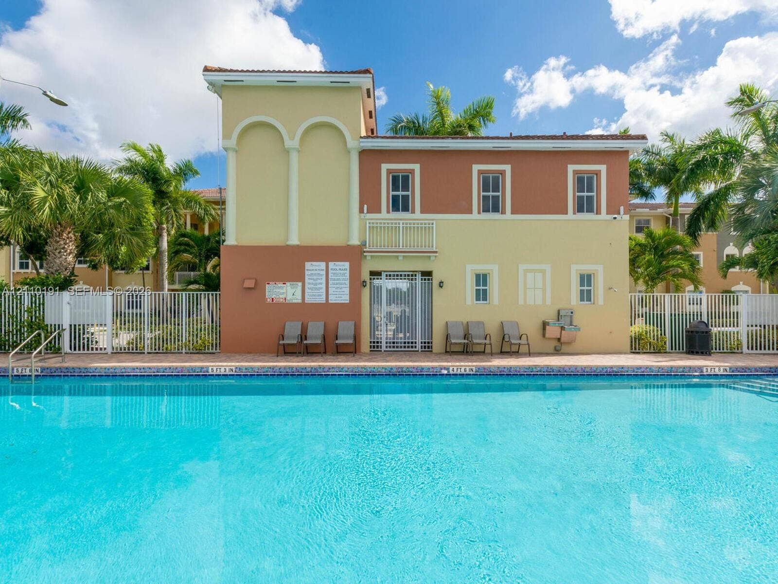 8999 NW 107 Court, #218-1, Miami, Miami, FL 33178 Swimming pool with tile edging, paver pool deck, two-story structure with stucco exterior, arched architectural detailing, and metal perimeter fencing