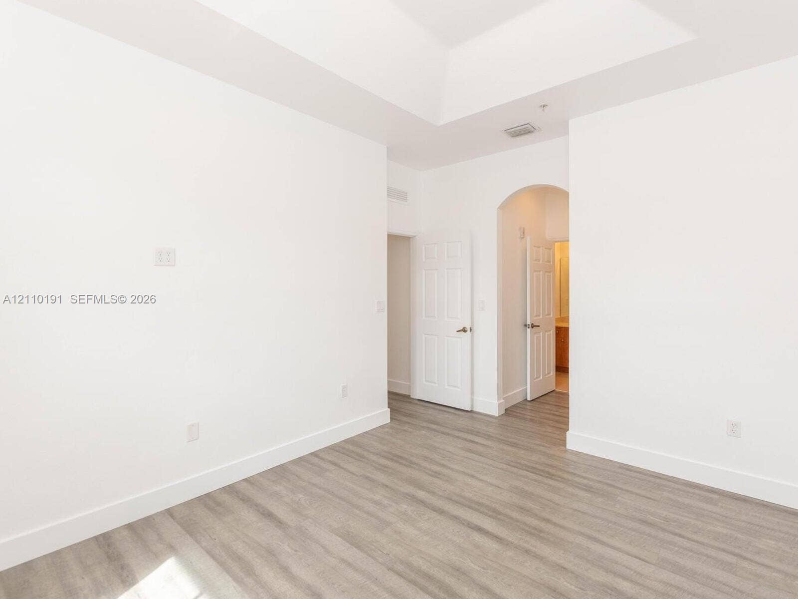 8999 NW 107 Court, #218-1, Miami, Miami, FL 33178 Interior space featuring wood-finish flooring, a tray ceiling, and an arched doorway leading to a secondary room