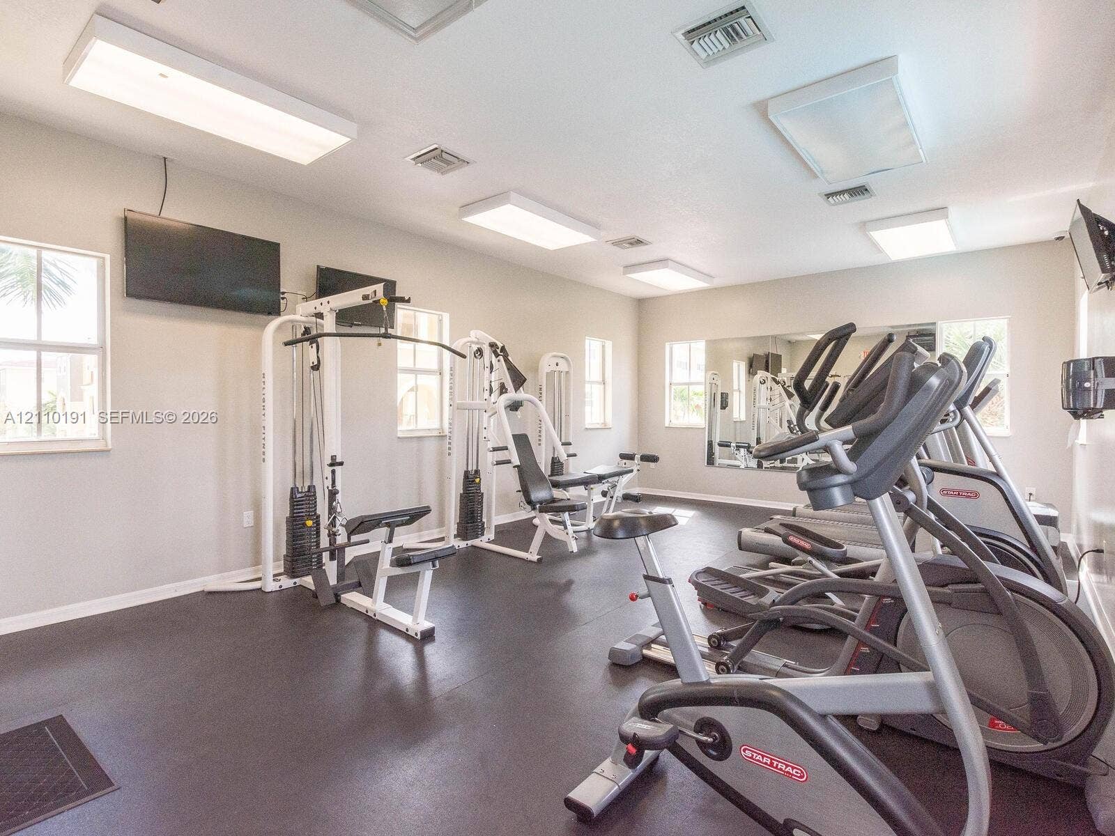 8999 NW 107 Court, #218-1, Miami, Miami, FL 33178 Fitness center featuring rubberized flooring, large wall-mounted mirrors, multiple overhead panel lights, and windows