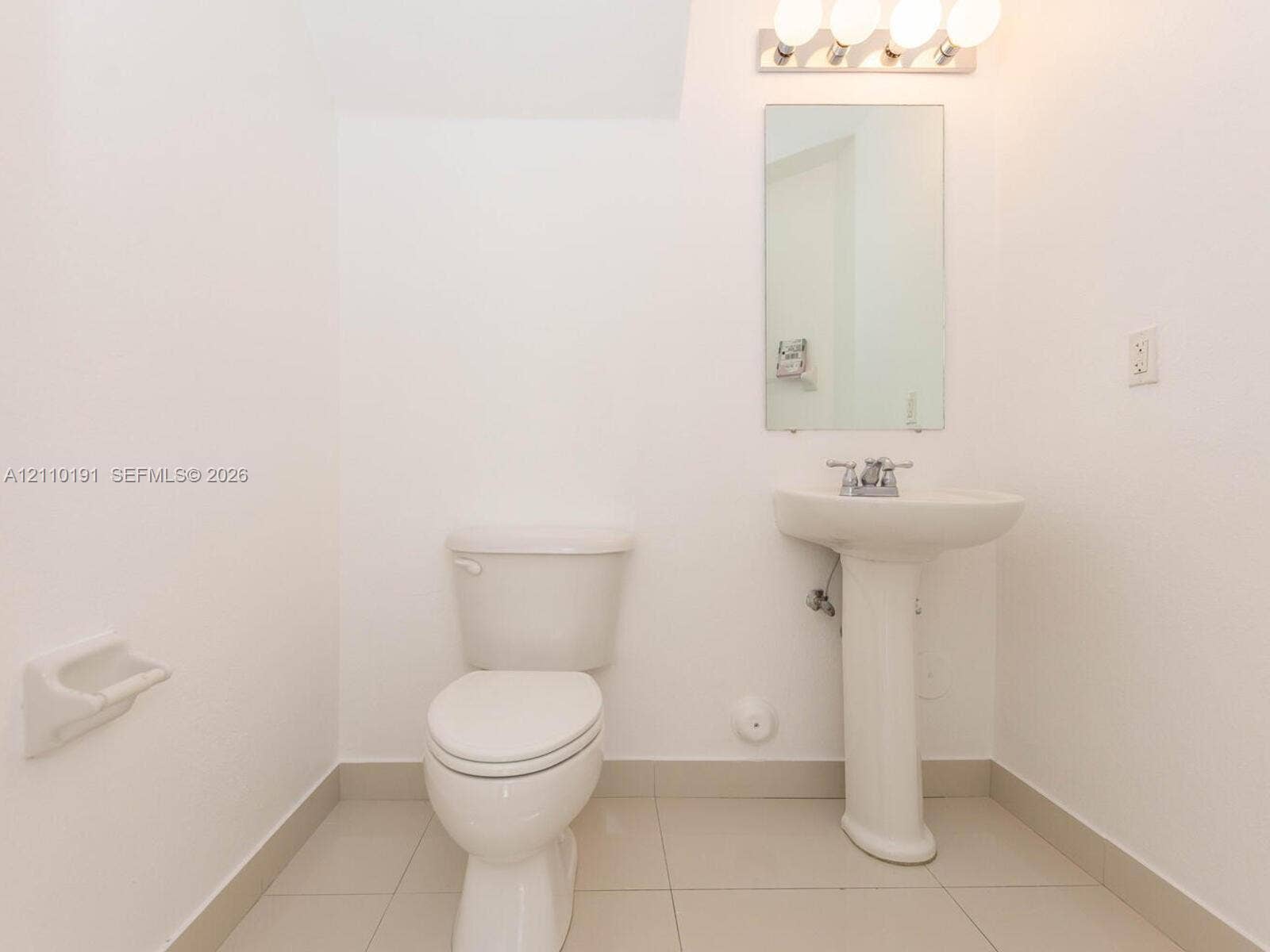 8999 NW 107 Court, #218-1, Miami, Miami, FL 33178 Bathroom featuring a white pedestal sink, dual-handle faucet, wall-mounted rectangular mirror, four-light vanity fixture, and tiled flooring