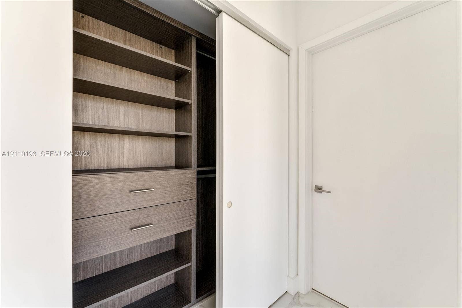 Built-in closet system featuring dark wood-finish shelving, two integrated storage drawers with metal hardware, a hanging rod, and a white sliding door