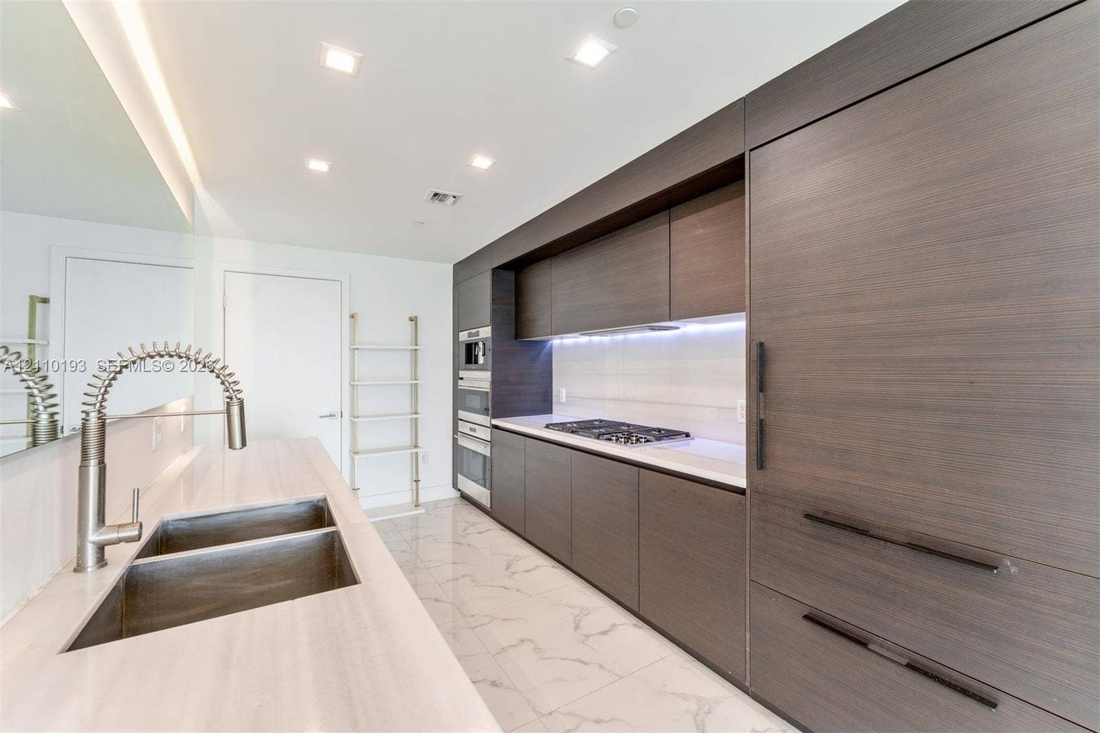 Modern kitchen featuring flat-panel wood-finish cabinetry, integrated built-in appliances, a dual-basin stainless steel sink with a spring-spout faucet, white stone countertops, and stone-finish floor tile