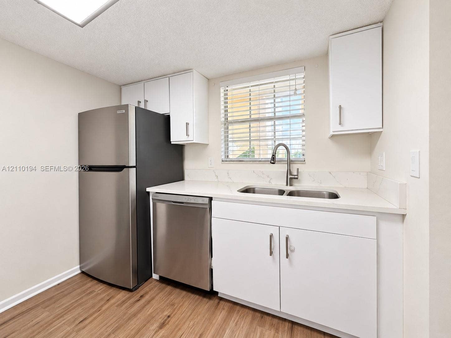 6331 La Costa Drive, #A, Boca Raton, Boca Raton, FL 33433 Kitchen featuring stainless steel refrigerator and dishwasher, white cabinetry, light-toned countertop with matching backsplash, and wood-finish flooring