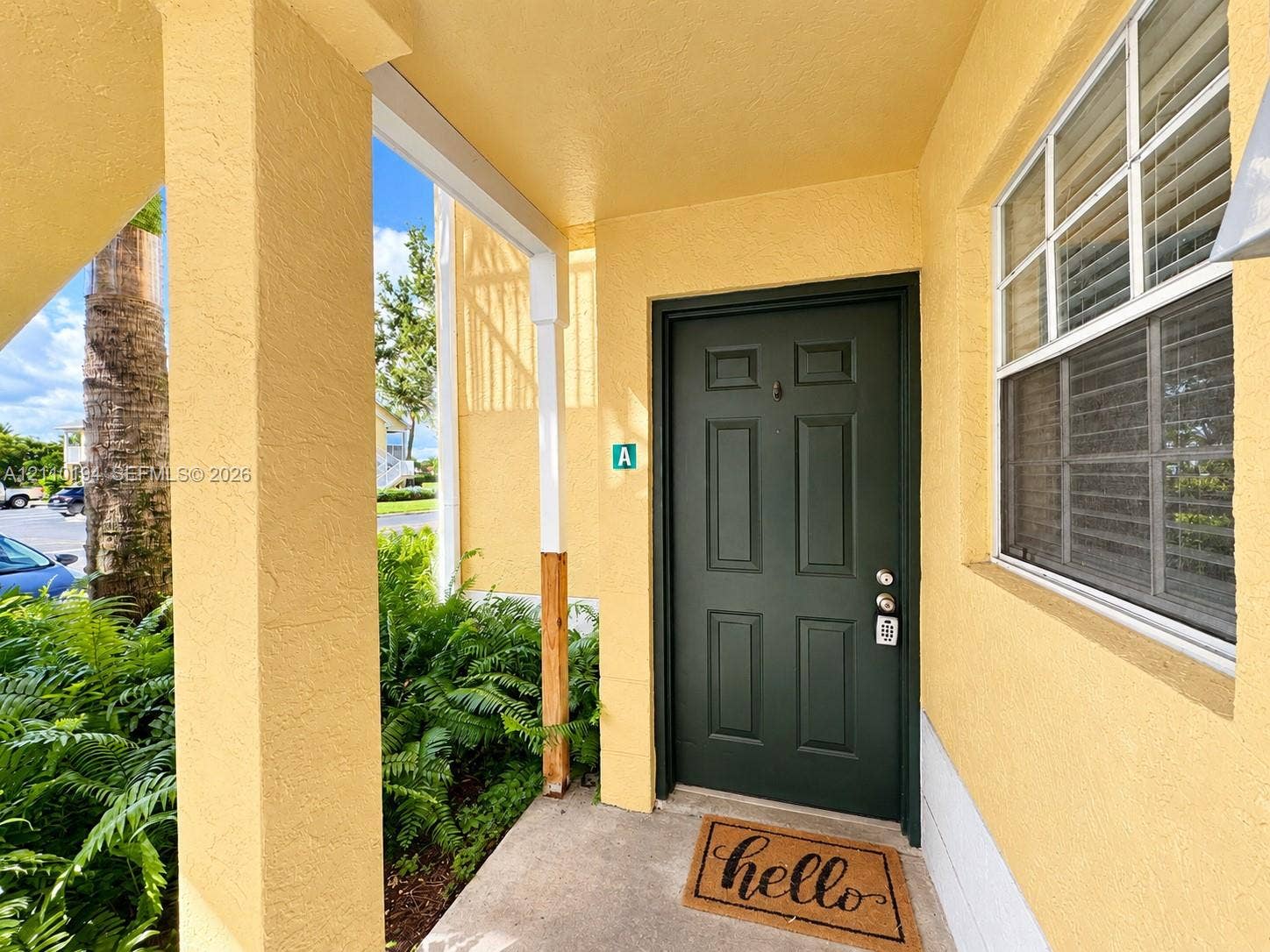 6331 La Costa Drive, #A, Boca Raton, Boca Raton, FL 33433 Covered entryway featuring a solid six-panel dark green door, structural column supports, and a single-hung window with a screen