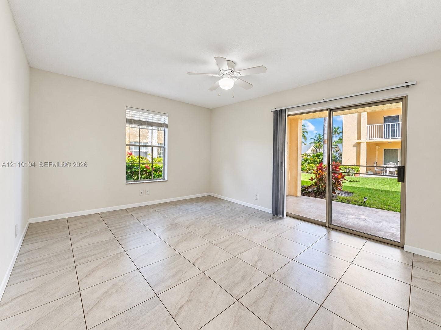 6331 La Costa Drive, #A, Boca Raton, Boca Raton, FL 33433 Neutral-toned interior space featuring large-format ceramic tile flooring, a ceiling fan with integrated lighting, and glass sliding doors providing access to a paved patio and outdoor space
