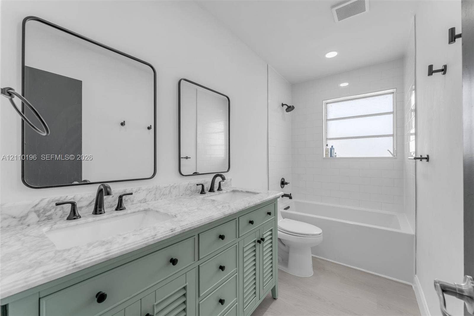 4400 SW 89th Avenue, #4400, Miami, Miami, FL 33165 Double vanity with stone-look countertop, green cabinetry with louvered door detailing, matte black fixtures, rectangular wall-mounted mirrors, and a tub-shower combination with white subway tile surround
