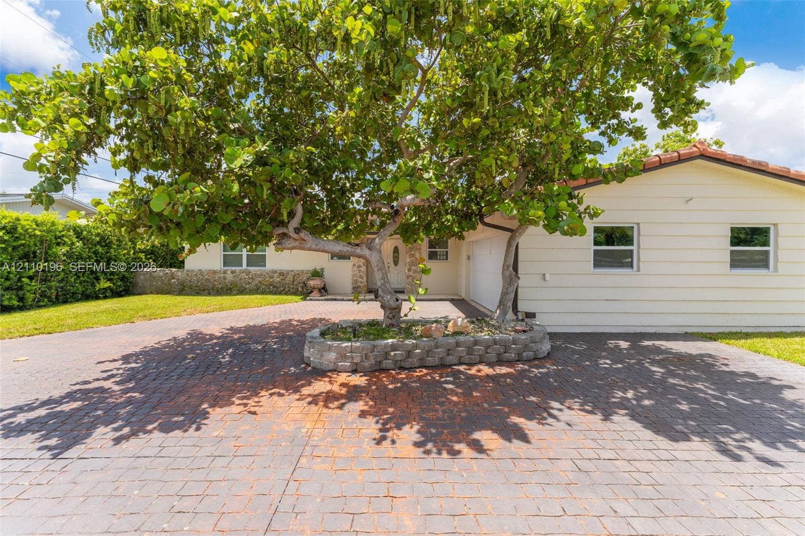 4400 SW 89th Avenue, #4400, Miami, Miami, FL 33165 Exterior featuring a multi-tone paved driveway, a centered raised stone planter with a mature tree, horizontal siding, and a tile roof