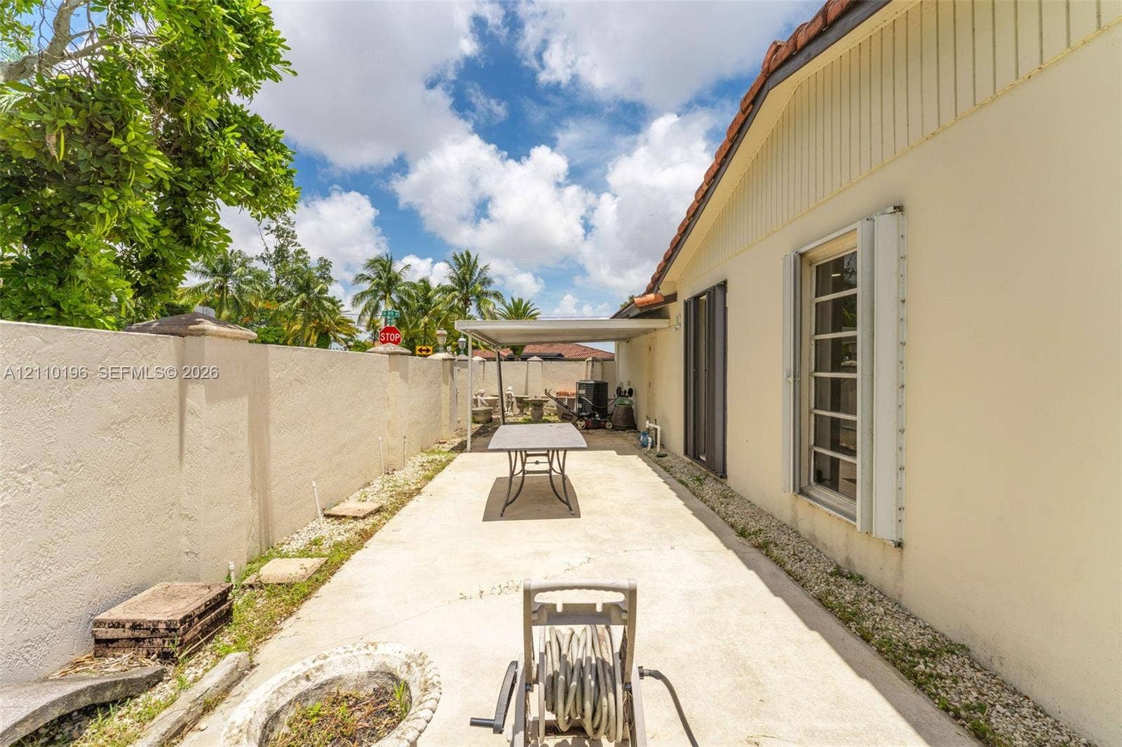 4400 SW 89th Avenue, #4400, Miami, Miami, FL 33165 Side patio featuring a concrete surface, enclosed by a solid masonry privacy wall, and partially shaded by a permanent metal awning