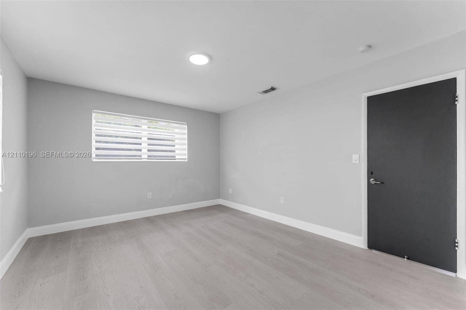 4400 SW 89th Avenue, #4400, Miami, Miami, FL 33165 Neutral-toned interior space featuring wood-finish flooring, light gray walls, and a contrasting dark-finished door with metallic hardware