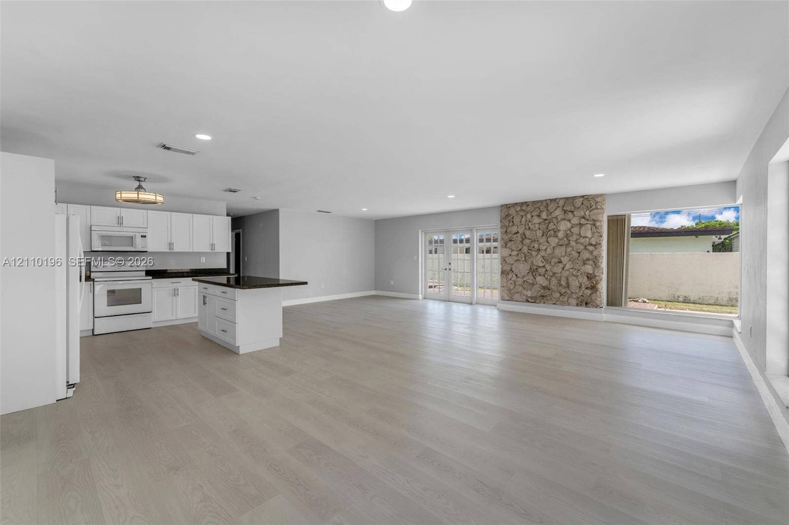 4400 SW 89th Avenue, #4400, Miami, Miami, FL 33165 Open-concept interior featuring wood-finish flooring, a kitchen with white cabinetry and dark countertops, a natural stone accent wall, recessed lighting, and glass-paneled double doors