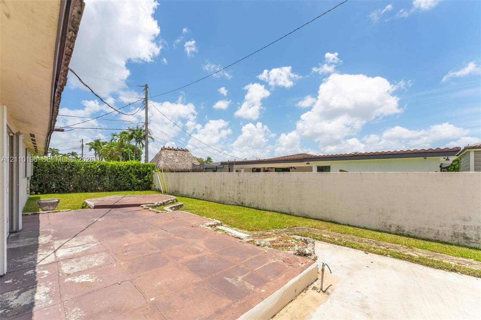 4400 SW 89th Avenue, #4400, Miami, Miami, FL 33165 Rear exterior space featuring a paved patio, elevated platform area, lawn, and perimeter masonry wall with hedge landscaping