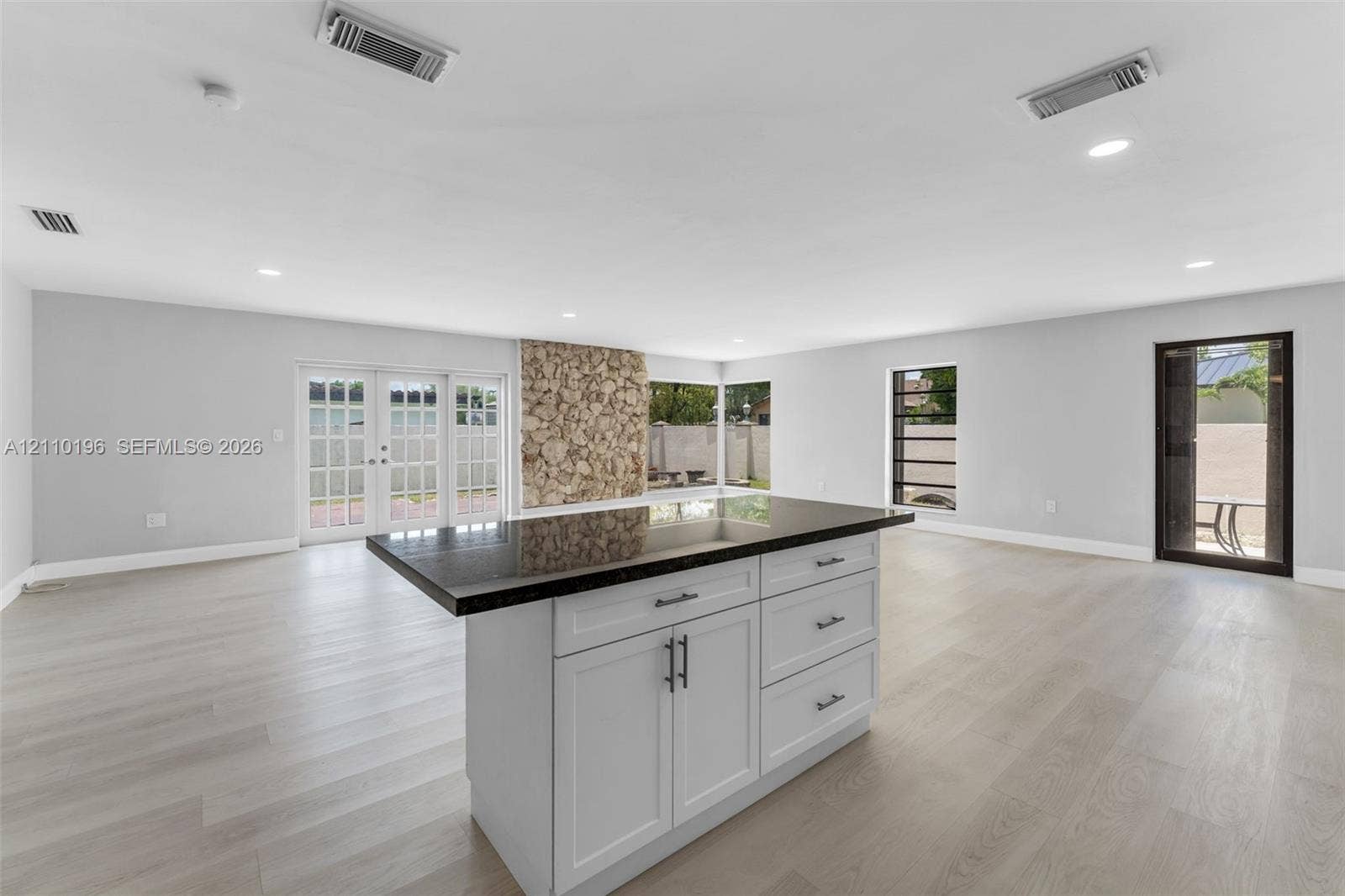 4400 SW 89th Avenue, #4400, Miami, Miami, FL 33165 Center island featuring shaker-style cabinetry, dark stone countertop, and recessed lighting, accented by a floor-to-ceiling natural stone feature wall and wood-finish flooring