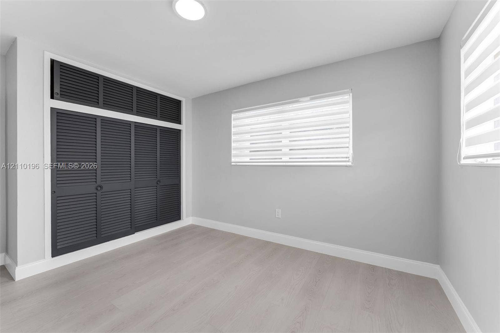 4400 SW 89th Avenue, #4400, Miami, Miami, FL 33165 Neutral-toned room featuring wood-finish flooring, built-in floor-to-ceiling louvered-style closet cabinetry with overhead storage, and dual windows with fitted horizontal blinds