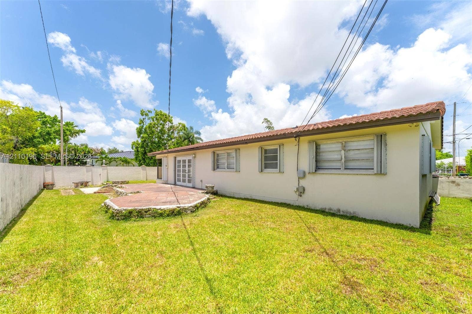 4400 SW 89th Avenue, #4400, Miami, Miami, FL 33165 Exterior of a single-story residence featuring light-colored stucco siding, a tiled roof, an elevated circular stone-finish patio, and a fenced backyard
