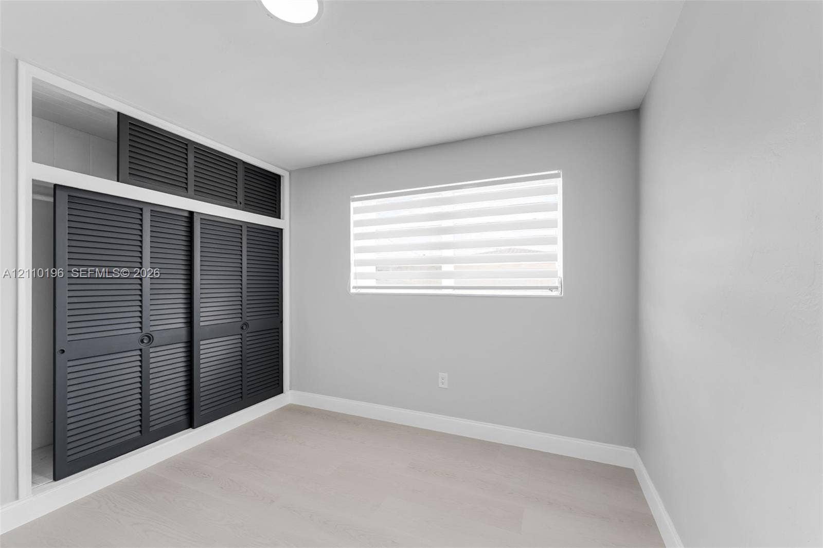 4400 SW 89th Avenue, #4400, Miami, Miami, FL 33165 Interior space featuring light-toned wood-finish flooring, charcoal-colored louvered sliding closet doors with built-in overhead storage, and dual-layered adjustable window blinds
