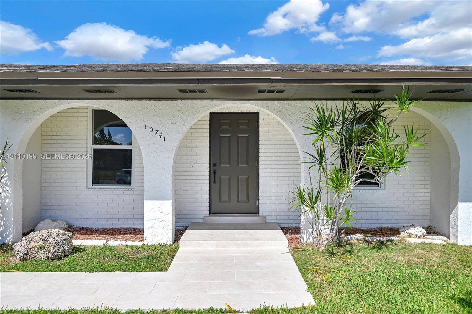 10741 SW 165th Street, Miami, FL 33157 Exterior facade featuring white painted brick, arched entryways, a paneled front door, and a light-toned stone pathway