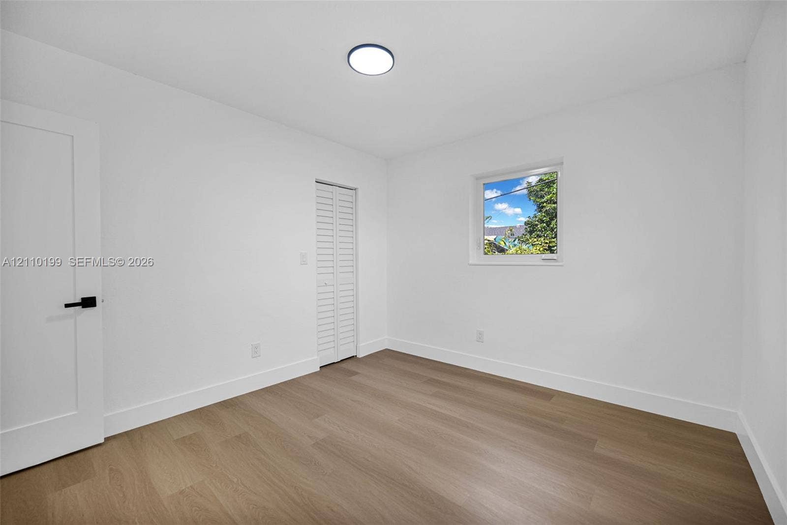10741 SW 165th Street, Miami, FL 33157 Interior space featuring wood-finish flooring, white walls, a single-window configuration, flush-mount lighting, and a closet with white louvered doors