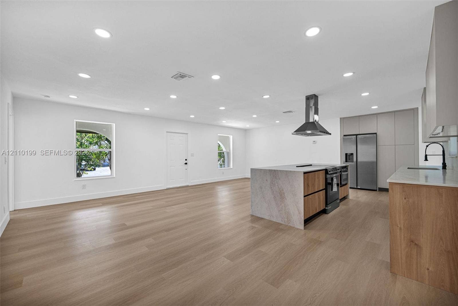 10741 SW 165th Street, Miami, FL 33157 Open-concept interior featuring light wood-finish flooring, recessed lighting, a kitchen island with stone-finish waterfall counters, flat-panel wood cabinetry, and stainless steel appliances including a range hood