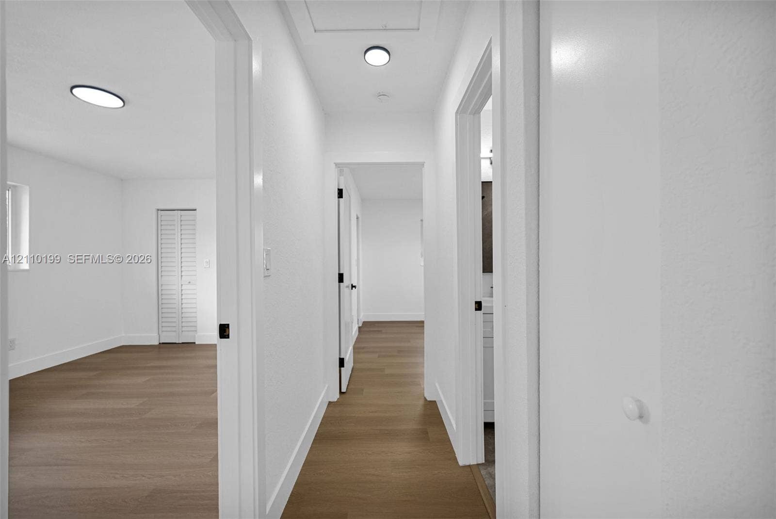 10741 SW 165th Street, Miami, FL 33157 Hallway featuring wood-finish flooring, white walls, flush-mount circular lighting, and louvered closet doors