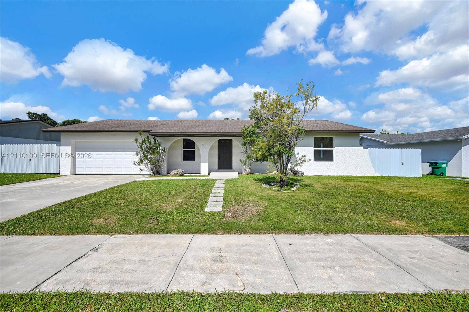 10741 SW 165th Street, Miami, FL 33157 Single-story exterior featuring a white painted brick facade, arched entryway, concrete driveway, and attached two-car garage