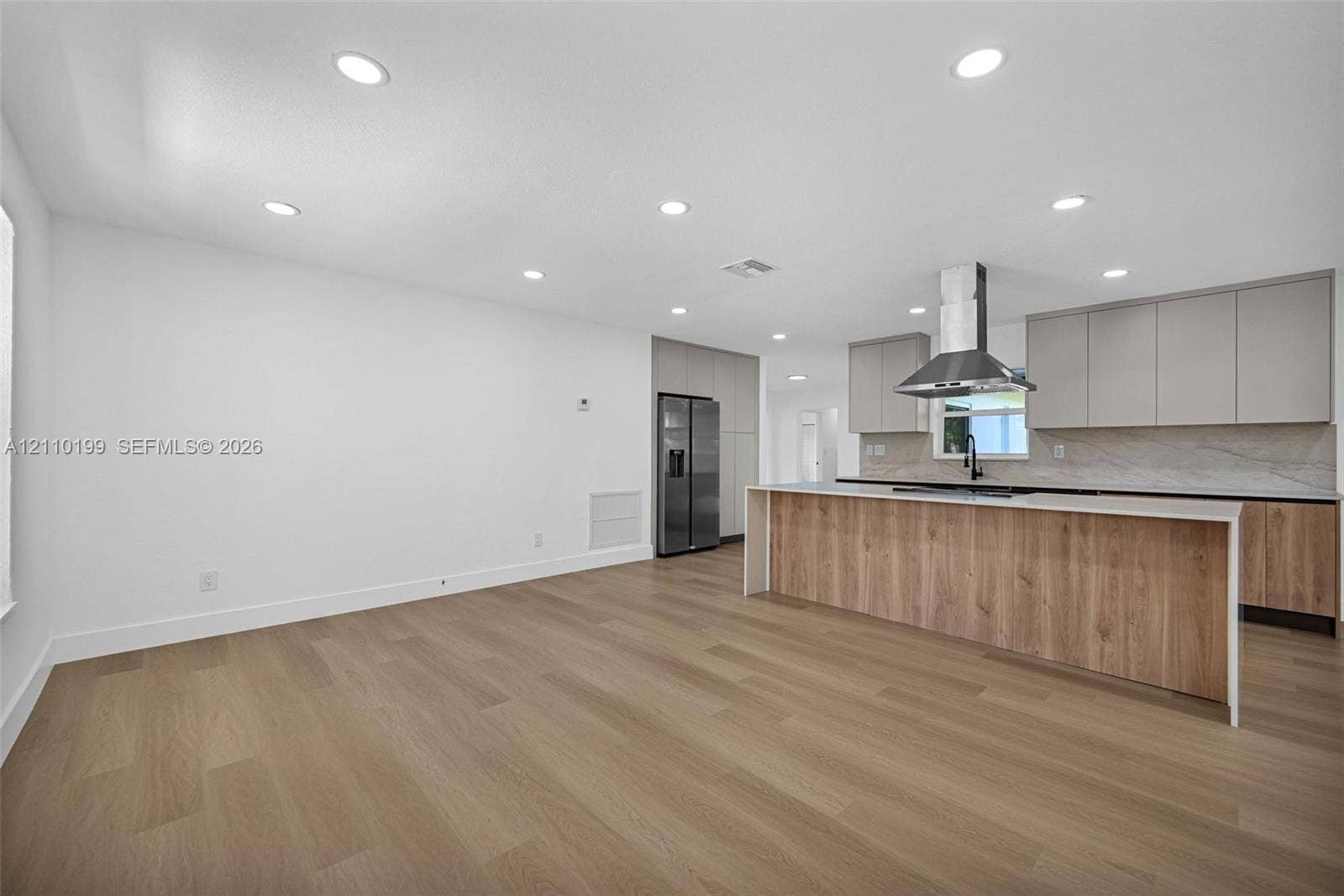 10741 SW 165th Street, Miami, FL 33157 Kitchen featuring wood-finish cabinetry, an island with a light-toned countertop, a stainless steel chimney-style range hood, integrated refrigerator, and wood-finish flooring