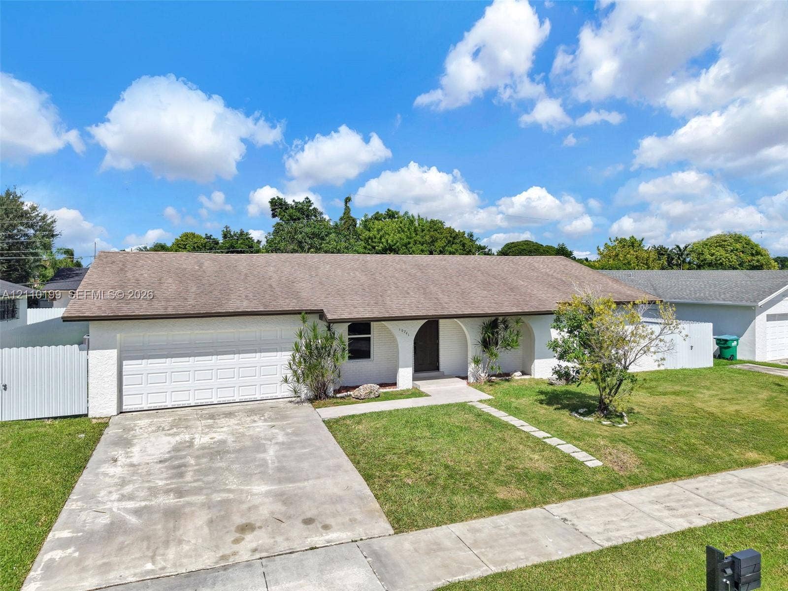 10741 SW 165th Street, Miami, FL 33157 Single-story exterior featuring white masonry walls, an arched covered entryway, a multi-car garage, and a concrete driveway