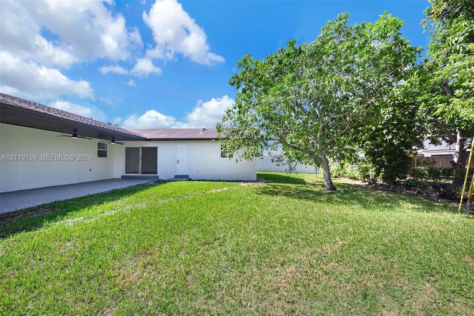 10741 SW 165th Street, Miami, FL 33157 Expansive backyard featuring a manicured lawn, mature trees, and a covered patio with integrated ceiling fans