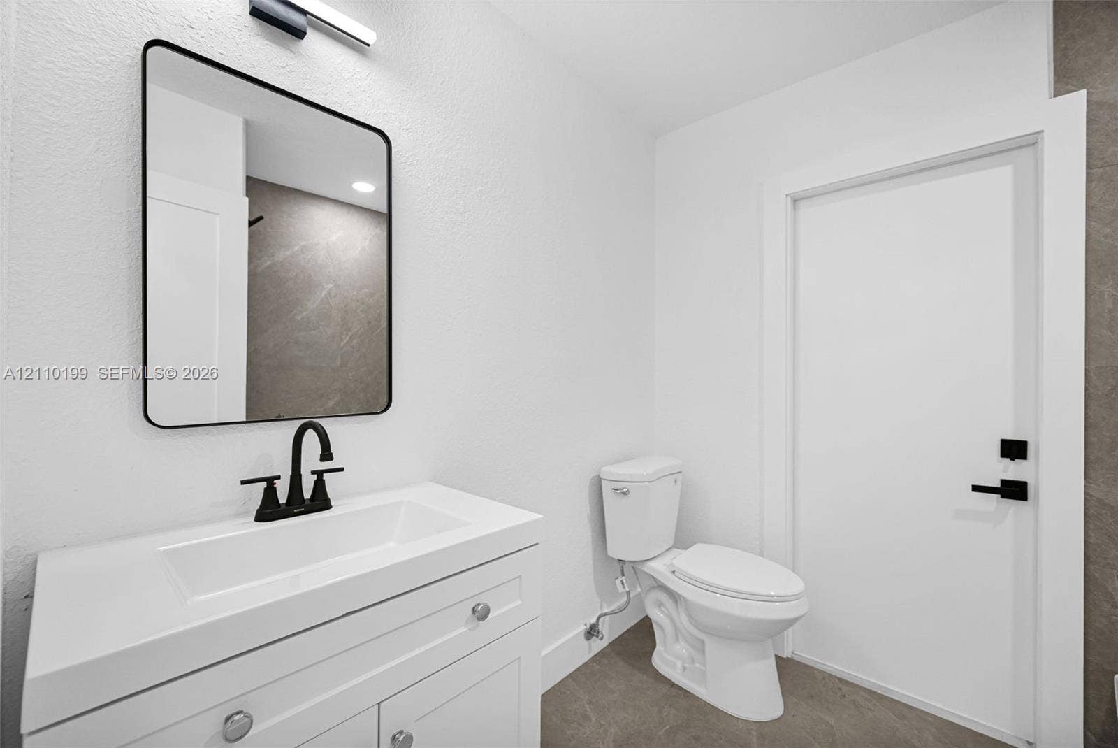 10741 SW 165th Street, Miami, FL 33157 White vanity featuring an integrated rectangular sink and stone-surface countertop, matte black faucet, rectangular mirror with a black frame, and matte black door hardware
