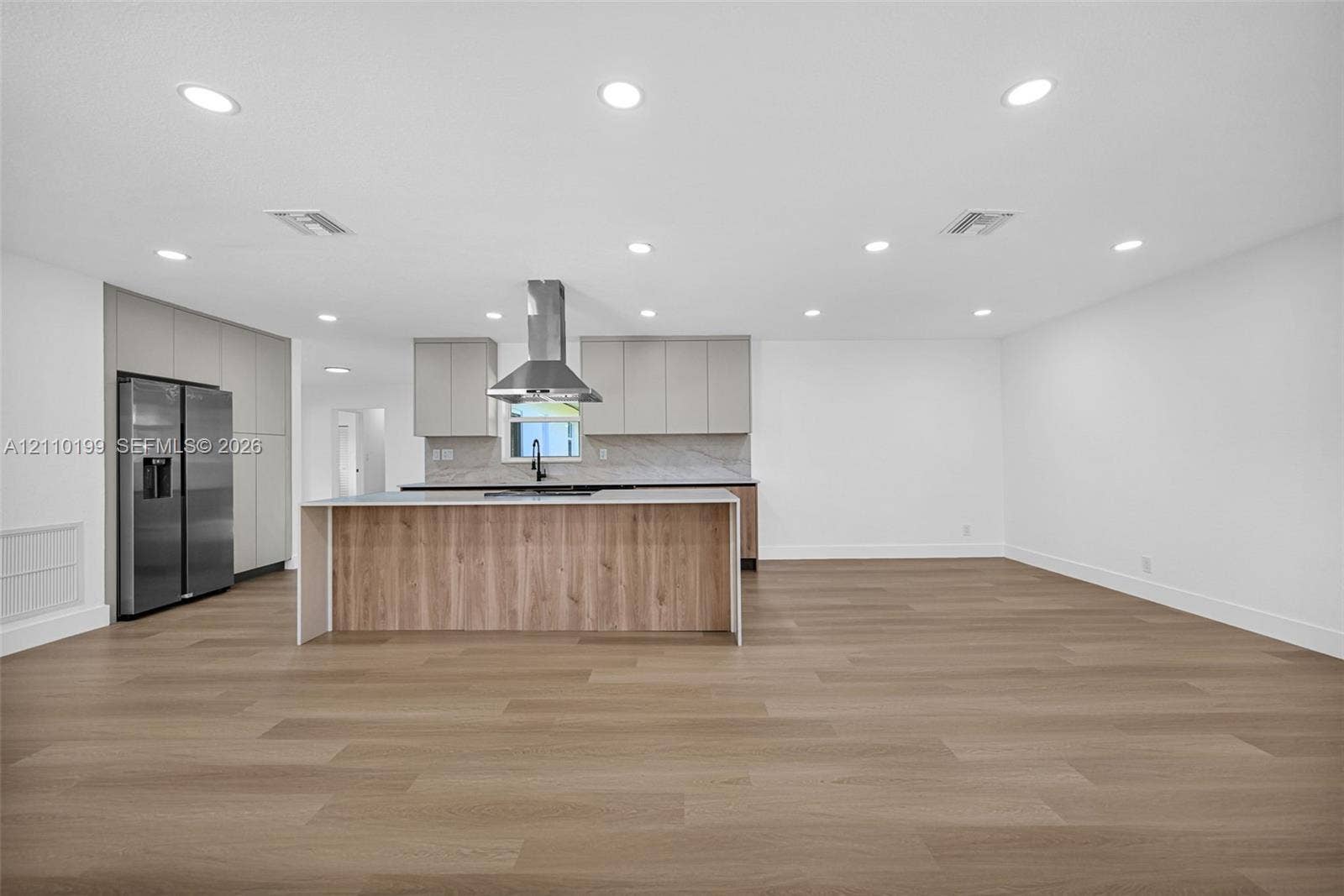 10741 SW 165th Street, Miami, FL 33157 Kitchen featuring flat-panel cabinetry, a central island with wood-finish paneling, a stainless steel chimney-style range hood, and wood-finish flooring throughout