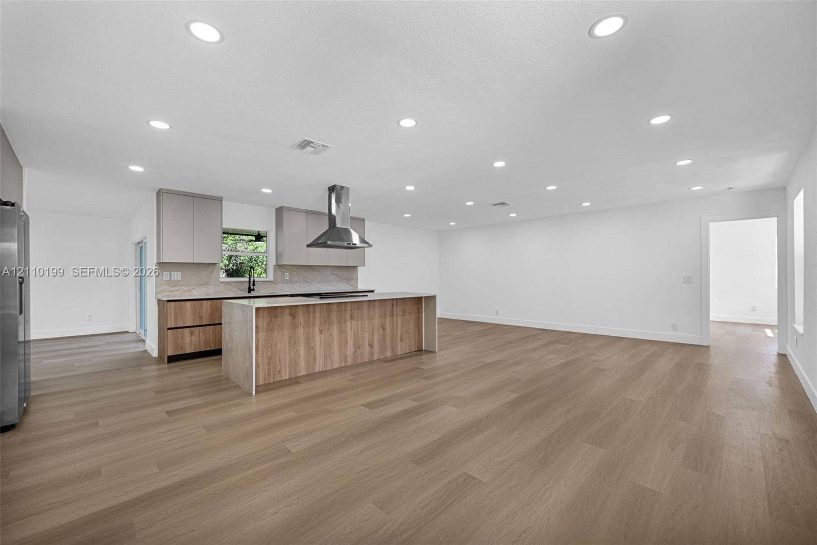 10741 SW 165th Street, Miami, FL 33157 Kitchen featuring flat-panel cabinetry, a center island with waterfall-edge countertop, stainless steel range hood, stone-finish backsplash, and wood-finish flooring