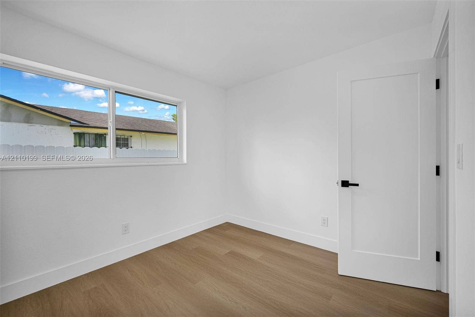 10741 SW 165th Street, Miami, FL 33157 Room featuring wood-finish flooring, a horizontal sliding window, and a white interior door with matte black hardware