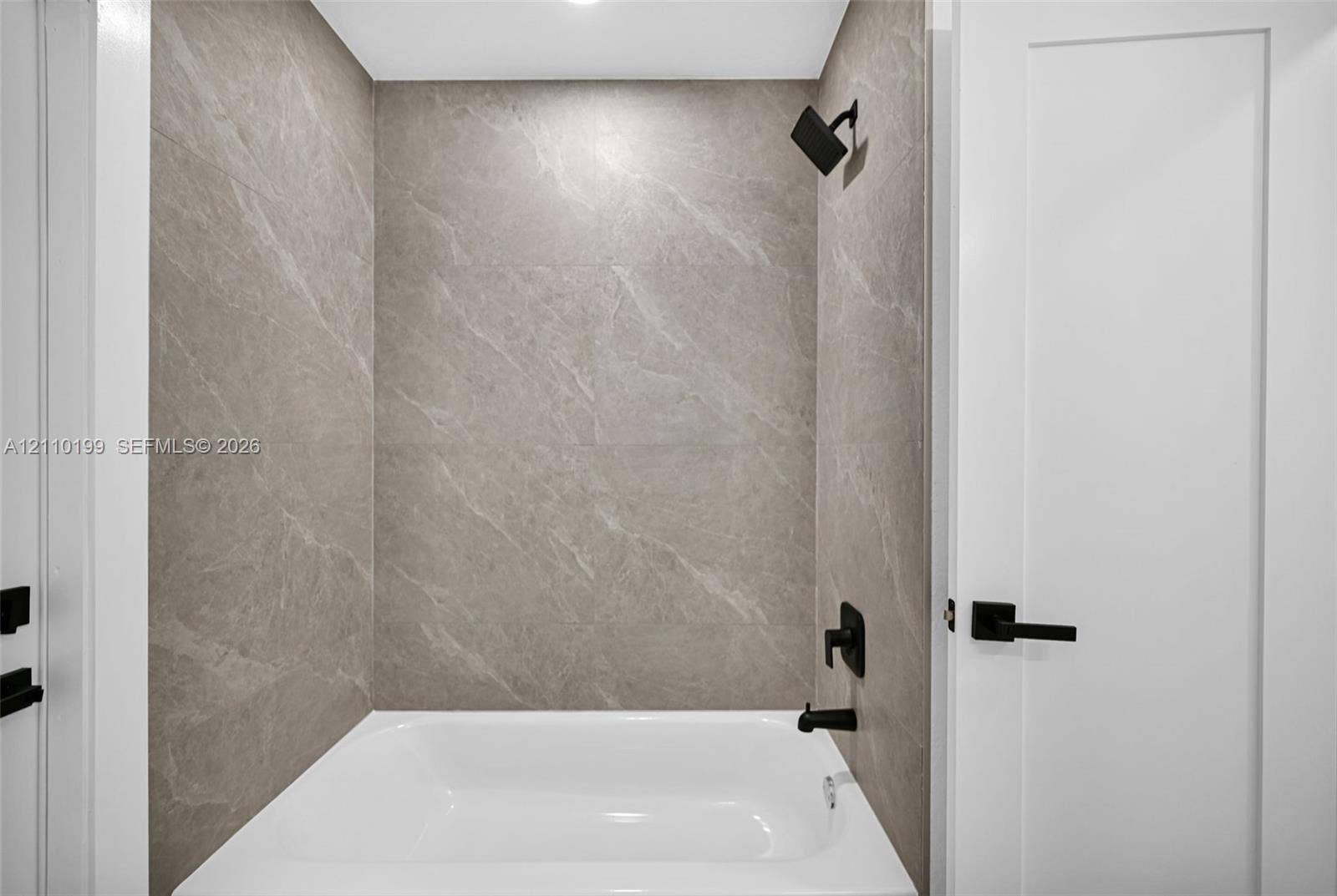 10741 SW 165th Street, Miami, FL 33157 Full-height neutral stone-finish tile surround, white soaking tub, and matte black plumbing fixtures