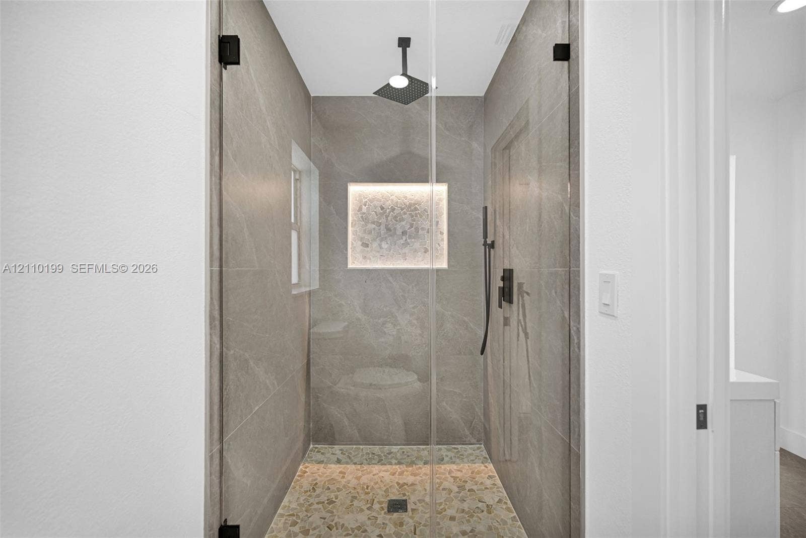 10741 SW 165th Street, Miami, FL 33157 Walk-in shower featuring large-format tile surround, frameless glass enclosure, rainfall showerhead, pebble-finish flooring, and a built-in recessed niche with integrated lighting