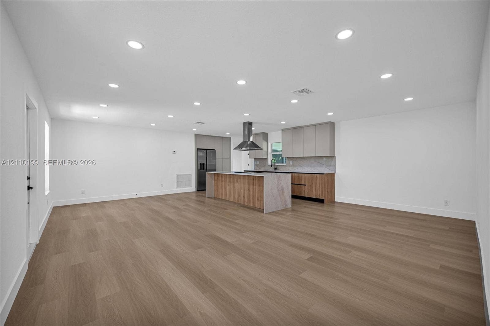 10741 SW 165th Street, Miami, FL 33157 Open-concept space featuring wood-finish flooring, recessed lighting, a center island with a stone-finish waterfall edge, two-tone cabinetry, and a stainless steel vent hood