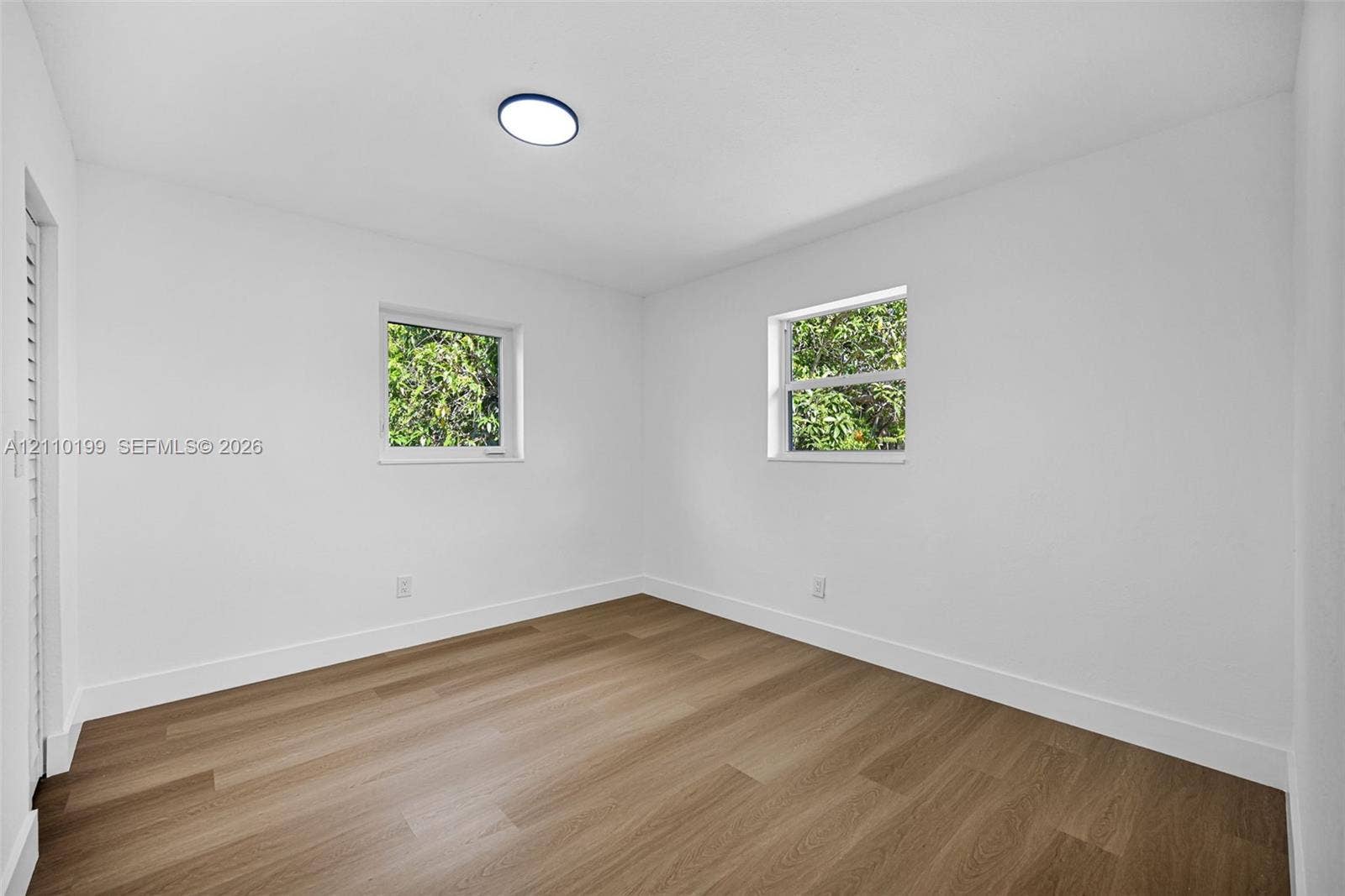 10741 SW 165th Street, Miami, FL 33157 Room featuring wood-finish flooring, white walls, dual windows, and a flush-mount ceiling light