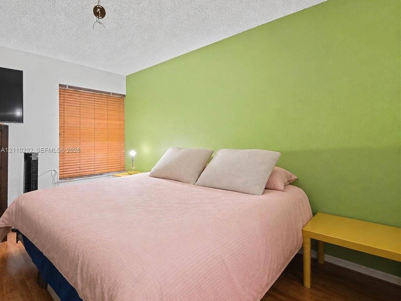 Room featuring wood-finish flooring, a textured ceiling, and a window fitted with horizontal blinds