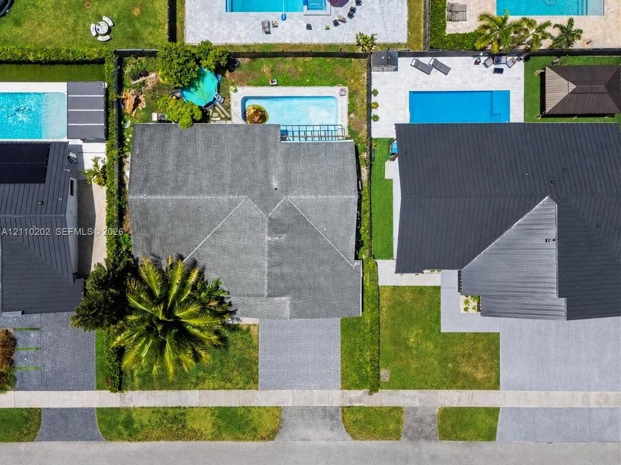 Aerial perspective of residential property featuring a backyard swimming pool, paved patio, perimeter fencing, and established palm landscaping