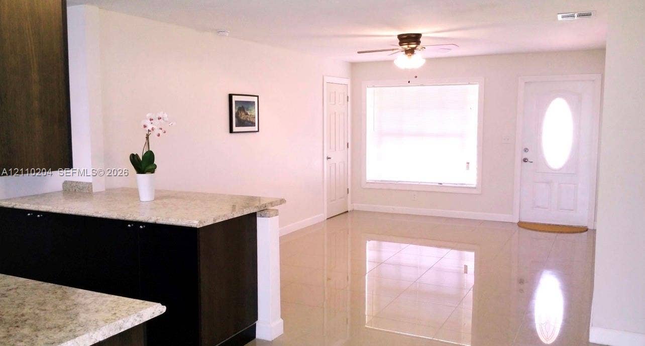 Kitchen featuring dark-finish cabinetry, stone-composite countertops, tile flooring, a ceiling fan with integrated lighting, and a front entry door with a glass inlay