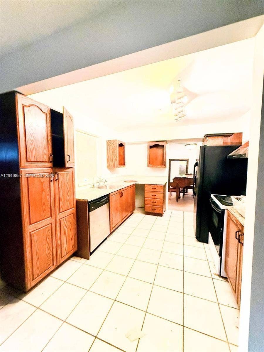 766 NW 24th Avenue, Delray Beach, FL 33445 Kitchen featuring wood cabinetry, integrated dishwasher, solid surface countertops, ceramic tile flooring, and black appliances