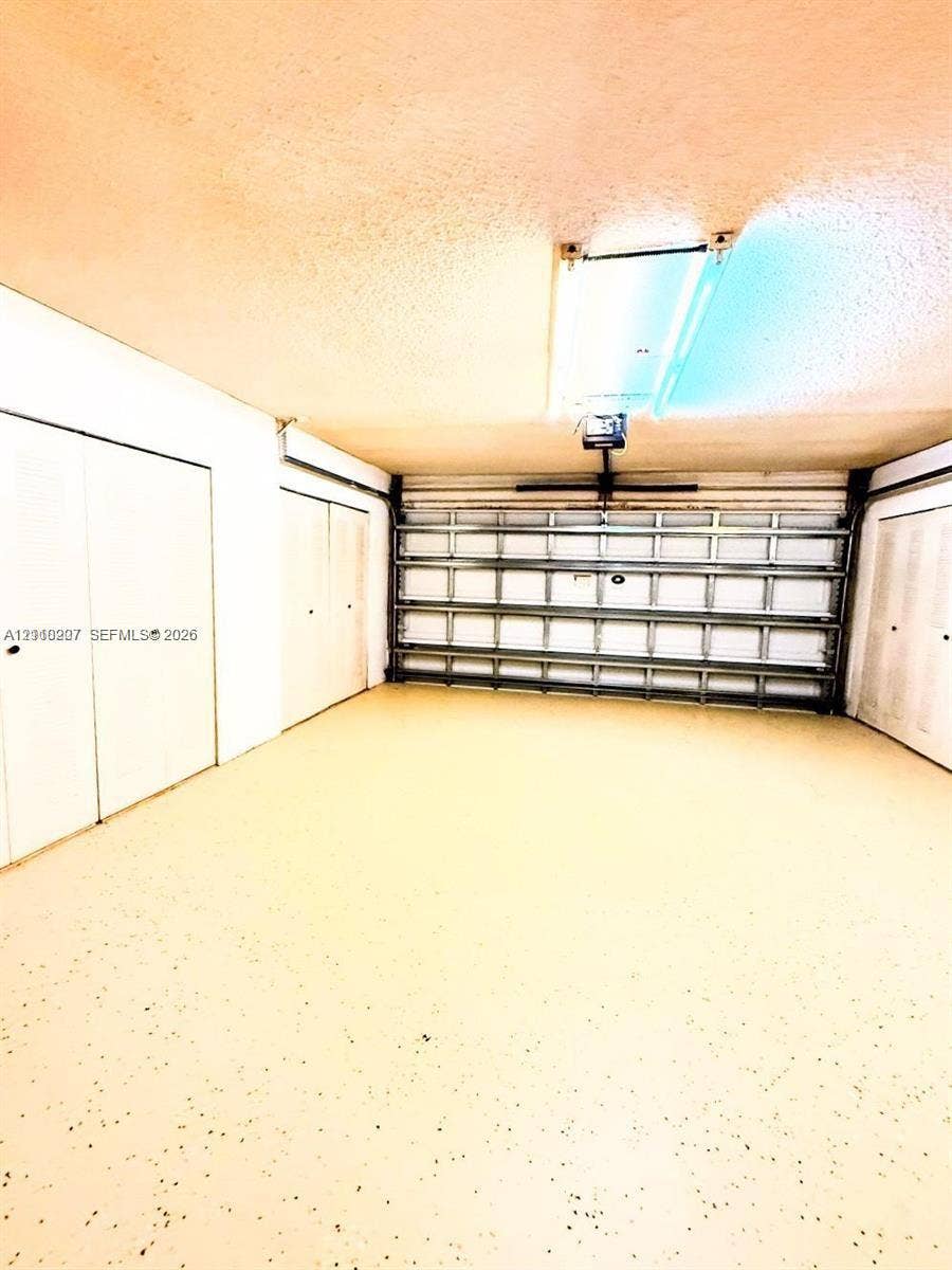 766 NW 24th Avenue, Delray Beach, FL 33445 Garage featuring an epoxy-coated floor, automatic sectional door, and three sets of double-door built-in storage closets