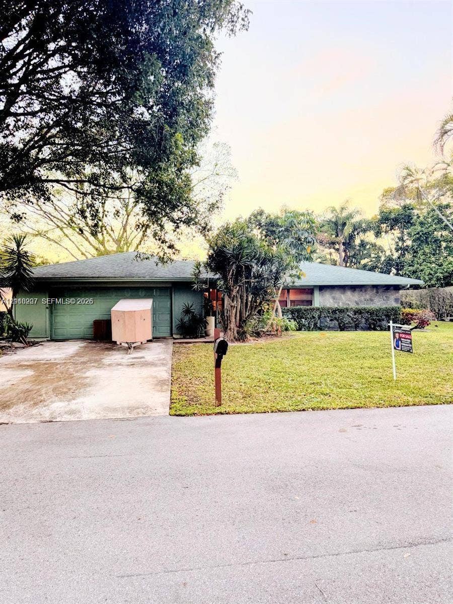 766 NW 24th Avenue, Delray Beach, FL 33445 Single-story residence featuring a low-slope roof, attached garage, stone-veneer exterior accents, and expansive front lawn with mature trees