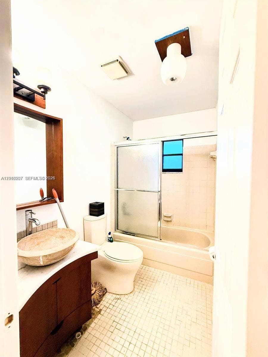 766 NW 24th Avenue, Delray Beach, FL 33445 Bathroom featuring a wood-finish vanity, stone vessel sink, framed mirror, and a combination bathtub and shower enclosure with sliding glass doors