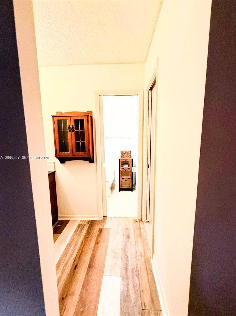 766 NW 24th Avenue, Delray Beach, FL 33445 Hallway featuring wood-finish flooring and a wall-mounted wood-finish cabinet with glass paneling